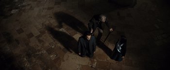 Movie still from “The Da Vinci Code” (2006), directed by Ron Howard – A man in a black suit is kneeling on the ground; Wide shot, Overhead angle