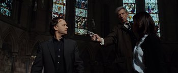 Movie still from “The Da Vinci Code” (2006), directed by Ron Howard – Two men in suits are holding guns in a church; Medium shot, Low angle
