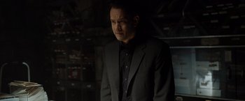 Movie still from “The Da Vinci Code” (2006), directed by Ron Howard – A man in a black suit standing in a dark room; Medium shot, Over the shoulder angle