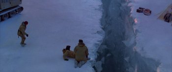 Movie still from “The Day After Tomorrow” (2004), directed by Roland Emmerich – Two people are sitting in the snow next to a body of water; Extreme Wide shot, Overhead angle