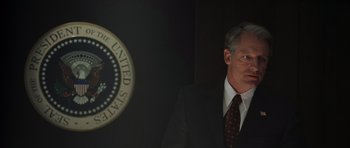 Movie still from “The Day After Tomorrow” (2004), directed by Roland Emmerich – A man in a suit and tie standing in front of a presidential seal; Medium shot, Low angle