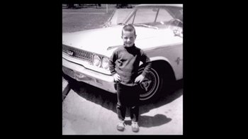 Movie still from “The Day the Music Died/American Pie” (2022), directed by Mark Moormann – A young boy standing in front of an old car; Wide shot, High angle