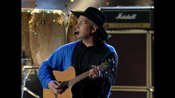 Movie still from “The Day the Music Died/American Pie” (2022), directed by Mark Moormann – A man in a cowboy hat is playing a guitar; Close Up shot, Low angle