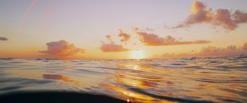 Movie still from “The Deepest Breath” (2023), directed by Laura McGann – The sun is setting over the ocean as seen from the water; Extreme Wide shot, Low angle