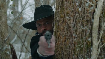 A man with a gun in his hand is leaning against a tree