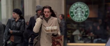 Movie still from “The Devil Wears Prada” (2006), directed by David Frankel – A woman walking down a street while holding a cup of coffee; Medium shot, Over the shoulder angle