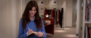 Movie still from “The Devil Wears Prada” (2006), directed by David Frankel – A woman writing in a notebook while standing in a room; Medium shot, Over the shoulder angle