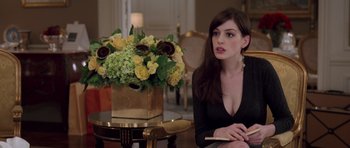 Movie still from “The Devil Wears Prada” (2006), directed by David Frankel – A woman sitting in front of a table with a vase filled with flowers; Medium shot, Over the shoulder angle