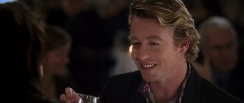 Movie still from “The Devil Wears Prada” (2006), directed by David Frankel – A person sitting at a table holding a glass; Close Up shot, Over the shoulder angle