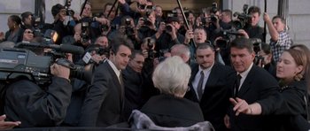 Movie still from “The Devil Wears Prada” (2006), directed by David Frankel – A group of people standing around a woman in front of a crowd; Medium shot, Over the shoulder angle