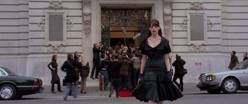A woman in a black dress is standing in front of a crowd of onlookers