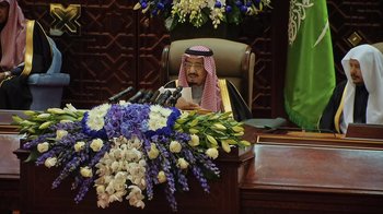 Movie still from “The Dissident” (2020), directed by Bryan Fogel – A man sitting at a desk with a bunch of flowers on top of it; Medium shot, Over the shoulder angle