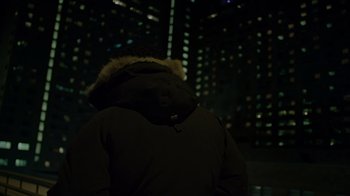 Movie still from “The Dissident” (2020), directed by Bryan Fogel – A person wearing a parka jacket in front of a city skyline at night; Medium shot, Low angle