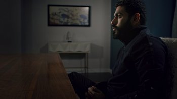 Movie still from “The Dissident” (2020), directed by Bryan Fogel – A man sitting at a table in front of a painting; Medium shot, High angle