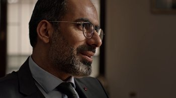 Movie still from “The Dissident” (2020), directed by Bryan Fogel – A person wearing glasses and a suit; Close Up shot, Over the shoulder angle