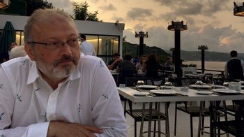 Movie still from “The Dissident” (2020), directed by Bryan Fogel – A man sitting at an outdoor table with a bunch of people in the background; Close Up shot, High angle