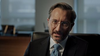 Movie still from “The Dissident” (2020), directed by Bryan Fogel – A man in a suit and tie sitting in an office chair; Close Up shot, Over the shoulder angle