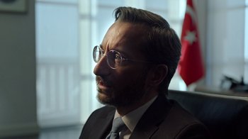 Movie still from “The Dissident” (2020), directed by Bryan Fogel – A person wearing glasses and a suit; Close Up shot, Over the shoulder angle