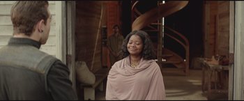 Movie still from “The Divergent Series: Insurgent” (2015), directed by Robert Schwentke – A woman in a pink dress is standing in front of a man in a brown suit; Medium shot, Over the shoulder angle