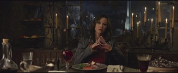 Movie still from “The Divergent Series: Insurgent” (2015), directed by Robert Schwentke – A woman sitting in front of a plate of food in front of candles; Medium shot, Over the shoulder angle