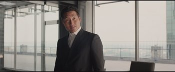 Movie still from “The Divergent Series: Insurgent” (2015), directed by Robert Schwentke – A man wearing a suit and tie standing in front of a window; Medium shot, Low angle