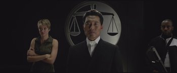 Movie still from “The Divergent Series: Insurgent” (2015), directed by Robert Schwentke – A man wearing a suit and tie standing in front of a sign; Medium shot, Low angle