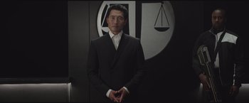 Movie still from “The Divergent Series: Insurgent” (2015), directed by Robert Schwentke – A man in a suit and tie standing in front of a law sign; Medium shot, Low angle