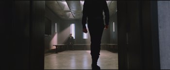 Movie still from “The Divergent Series: Insurgent” (2015), directed by Robert Schwentke – A man walking in a room with a man sitting in a chair in front of him; Wide shot, Over the shoulder angle