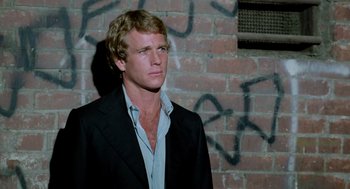 Movie still from “The Driver” (1978), directed by Walter Hill – A man wearing a suit and tie standing in front of a brick wall; Close Up shot, Low angle