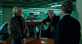 Movie still from “The Driver” (1978), directed by Walter Hill – A group of people standing next to each other in front of a car; Medium shot, Over the shoulder angle