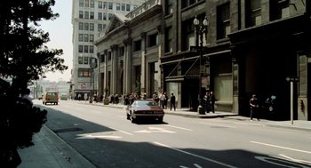 Movie still from “The Driver” (1978), directed by Walter Hill – A car driving down a street past a tall building; Extreme Wide shot, High angle