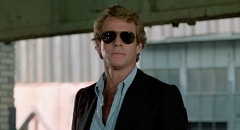 Movie still from “The Driver” (1978), directed by Walter Hill – A person wearing a suit and sunglasses; Close Up shot, Low angle
