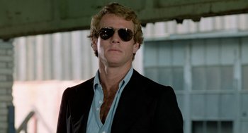 Movie still from “The Driver” (1978), directed by Walter Hill – A person wearing a suit and sunglasses; Close Up shot, Low angle