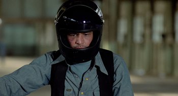 Movie still from “The Driver” (1978), directed by Walter Hill – A man wearing a black motorcycle helmet and a blue shirt; Medium shot, Low angle