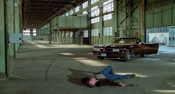 Movie still from “The Driver” (1978), directed by Walter Hill – A man laying on the ground next to a car; Wide shot, High angle