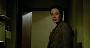 Movie still from “The Driver” (1978), directed by Walter Hill – A woman standing in a dark room wearing a suit and red tie; Close Up shot, Over the shoulder angle