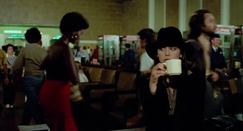 Movie still from “The Driver” (1978), directed by Walter Hill – A woman in a black hat drinking a cup of coffee; Medium shot, Over the shoulder angle