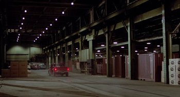 Movie still from “The Driver” (1978), directed by Walter Hill – A red truck driving down a street next to a building; Extreme Wide shot, High angle
