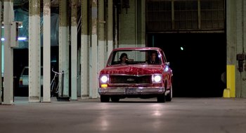 Movie still from “The Driver” (1978), directed by Walter Hill – Two people sitting in the driver's seat of an old red car; Wide shot, Over the shoulder angle