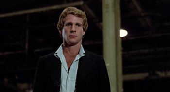 Movie still from “The Driver” (1978), directed by Walter Hill – A man in a black jacket and white shirt; Close Up shot, Low angle