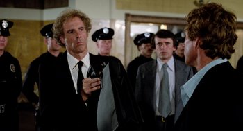 Movie still from “The Driver” (1978), directed by Walter Hill – A group of men standing next to each other in a room; Medium shot, Over the shoulder angle