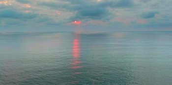 Movie still from “The Drop” (2022), directed by Sarah Adina Smith – The sun is setting over the ocean on a cloudy day; Extreme Wide shot, High angle