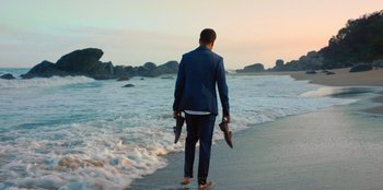 A man walking on the beach holding two umbrellas