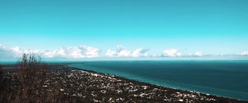 Movie still from “The Dunes” (2021), directed by Martin Copping – A view of the ocean from a hill above a city; Extreme Wide shot, High angle