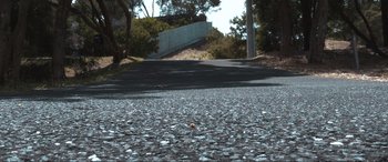 Movie still from “The Dunes” (2021), directed by Martin Copping – A road that has some trees and a bridge in the background; Extreme Wide shot, Low angle