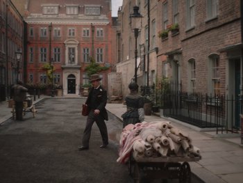 Movie still from “The Electrical Life of Louis Wain” (2021), directed by Will Sharpe – A man in a suit and hat pushing a cart full of logs; Wide shot, High angle
