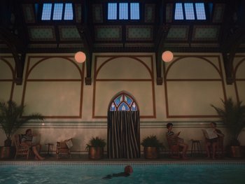 Movie still from “The Electrical Life of Louis Wain” (2021), directed by Will Sharpe – A woman swimming in a swimming pool with chairs around it; Extreme Wide shot, High angle