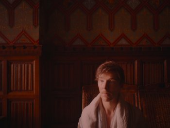 Movie still from “The Electrical Life of Louis Wain” (2021), directed by Will Sharpe – A man sitting in a chair with a towel around his neck; Medium shot, High angle