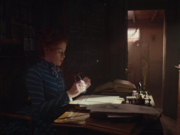 Movie still from “The Electrical Life of Louis Wain” (2021), directed by Will Sharpe – A woman sitting at a desk with papers and a phone; Medium shot, Over the shoulder angle