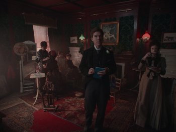 Movie still from “The Electrical Life of Louis Wain” (2021), directed by Will Sharpe – A man in a suit and tie in a living room; Wide shot, Low angle